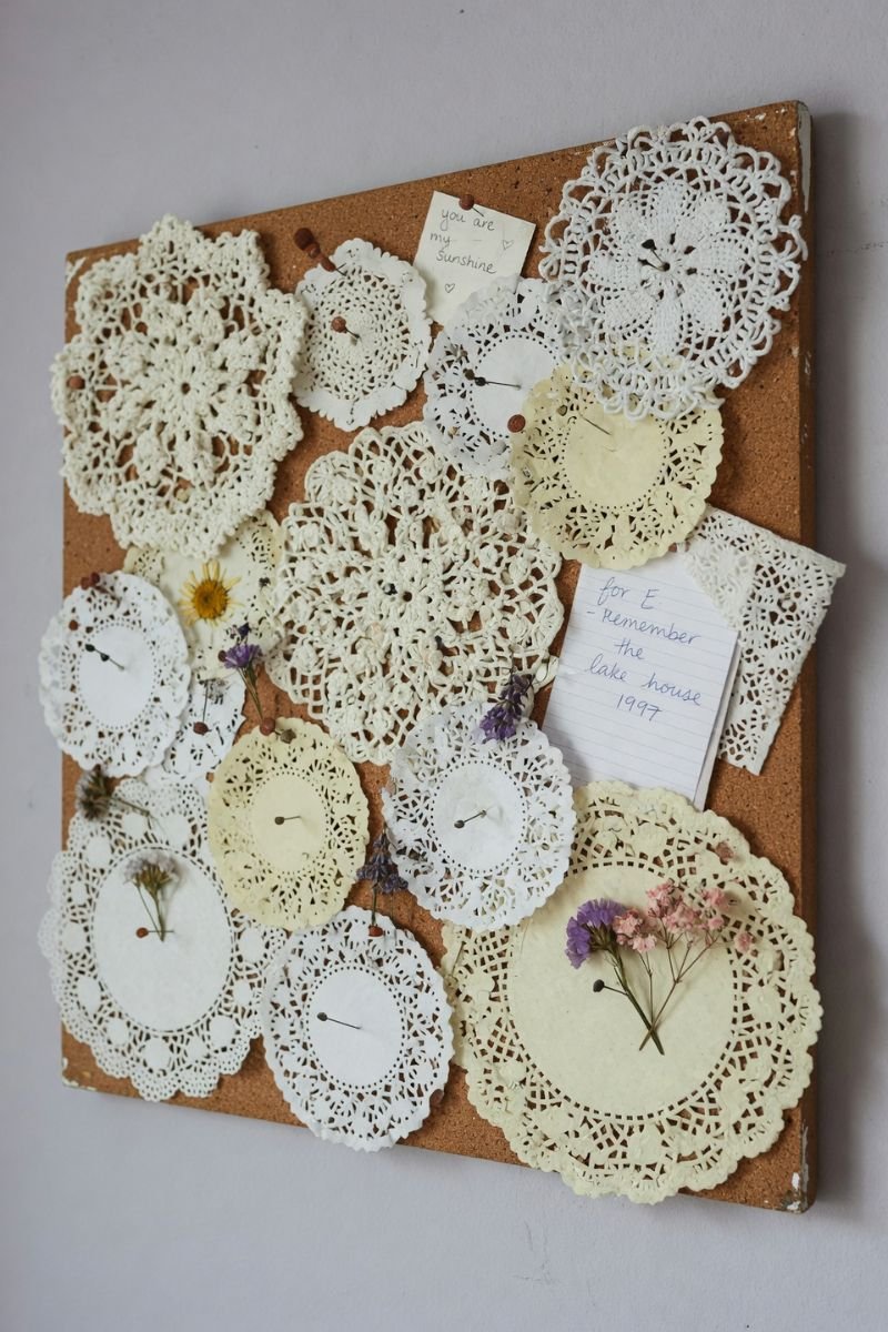 Corkboard gallery wall covered with overlapping white doilies and dried flowers