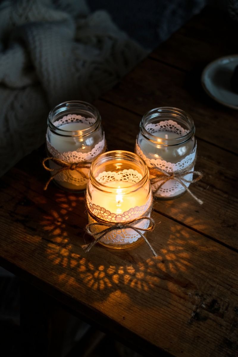 Glass candle jars wrapped in white doilies with twine on a wooden surface