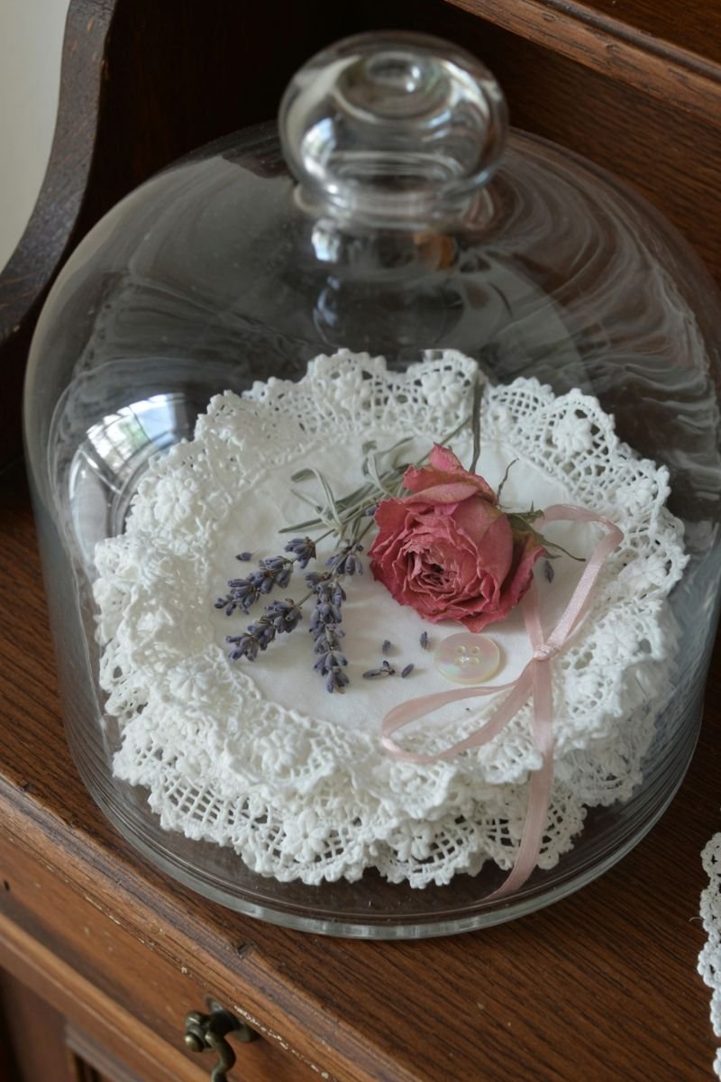Glass cloche with folded white doily and dried flowers on a wooden dresser
