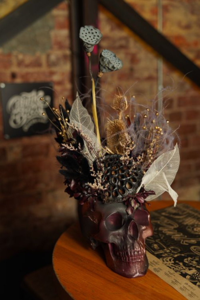 Halloween table centerpiece with dried dark florals, decorative skull, and burgundy candles