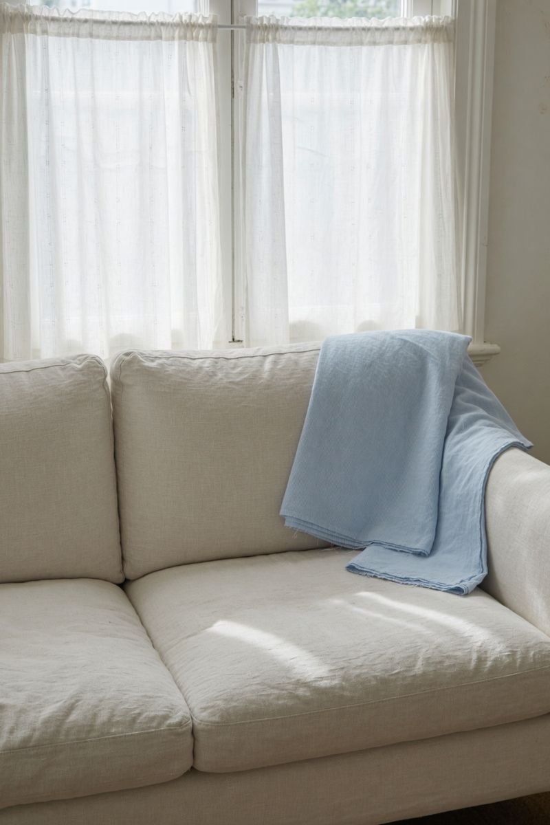 Lightweight pale blue cotton throw folded over sofa armrest in summer living room