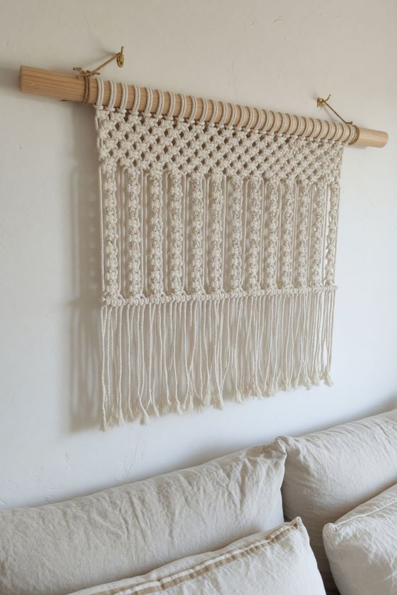 Natural cotton macrame wall hanging above a linen sofa on a white wall