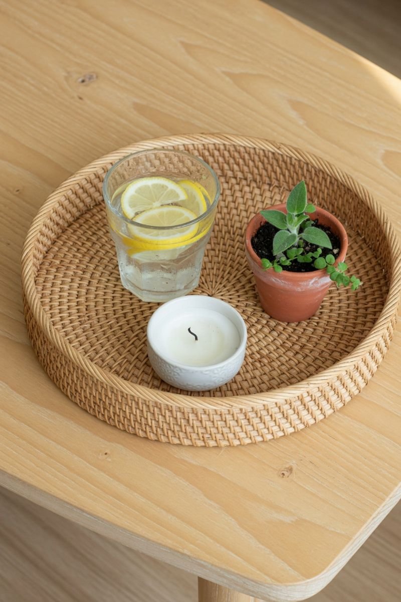 Round rattan tray on coffee table styled with lemon water candle and small plant