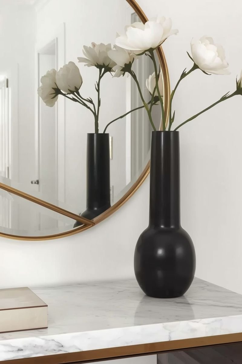 Sculptural black ceramic vase on a marble console table in front of a gold mirror