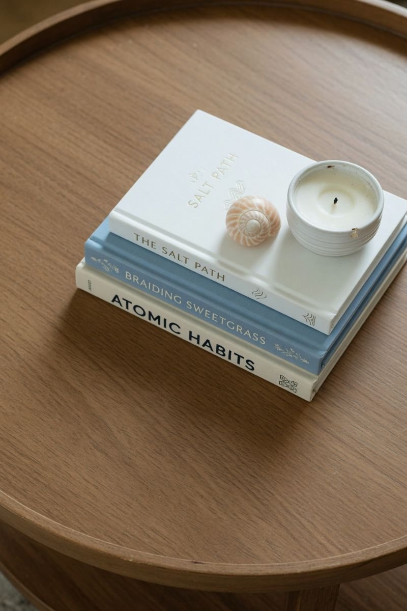 Stack of white blue and cream books on a coffee table with a shell and candle
