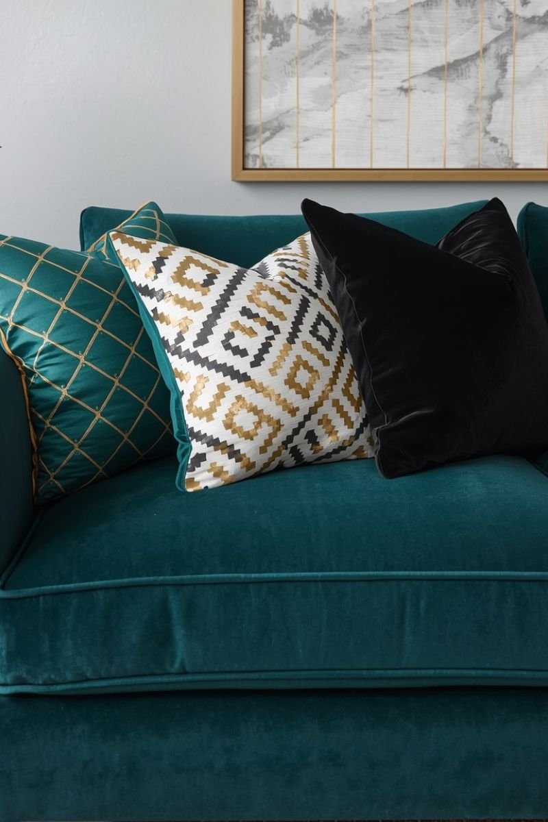 Three geometric throw pillows in gold black and ivory on a navy velvet sofa