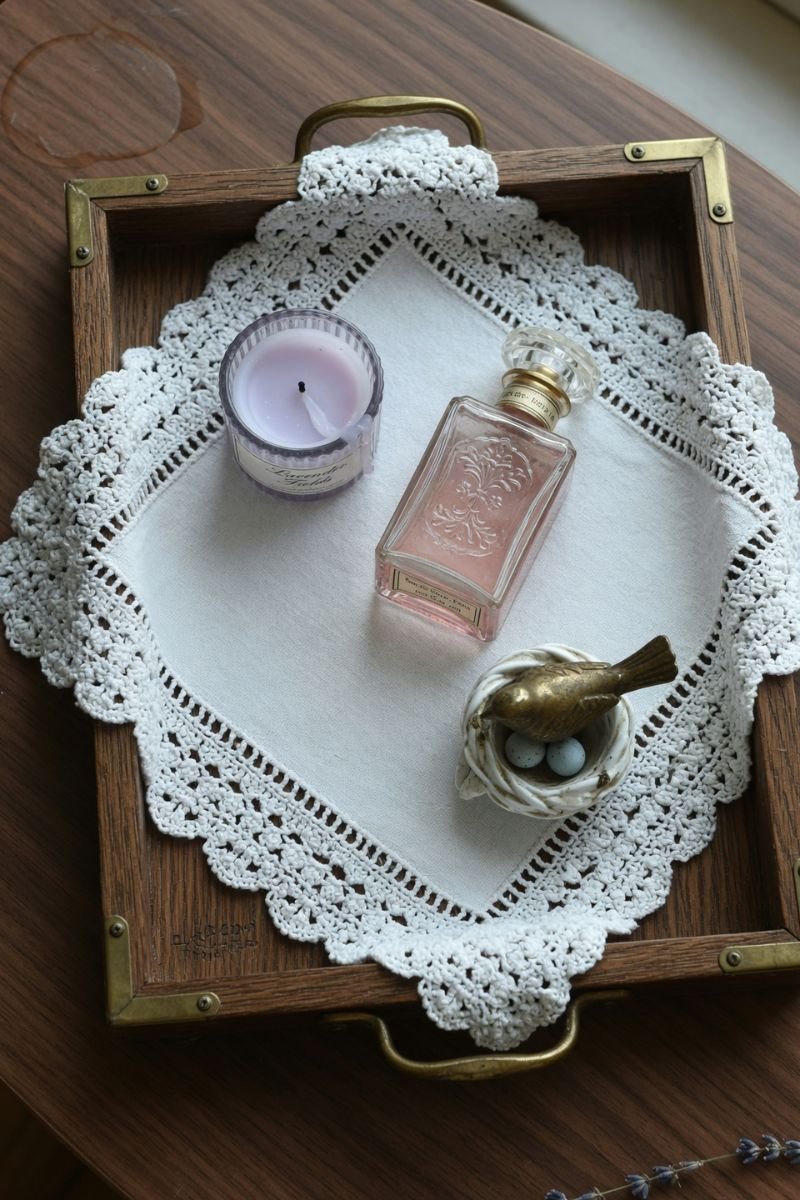 White doily lining a wooden tray with candle and small decor objects