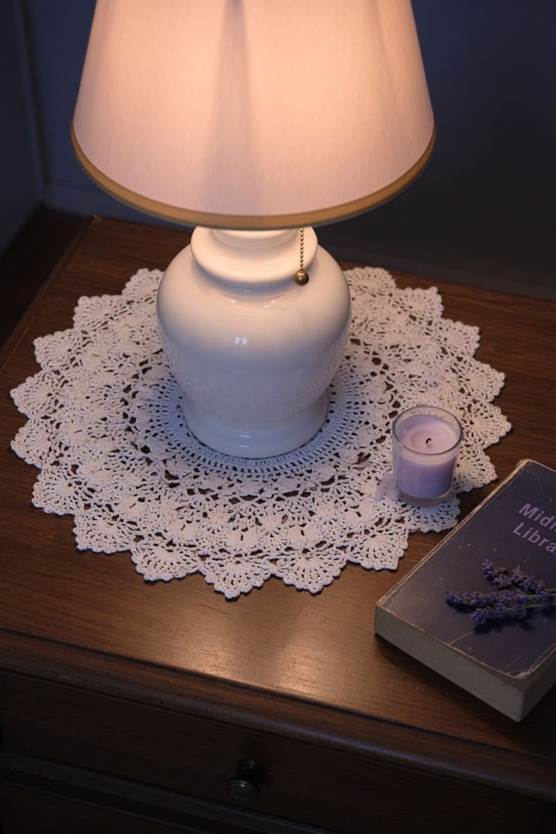 White doily under ceramic table lamp on a wooden nightstand