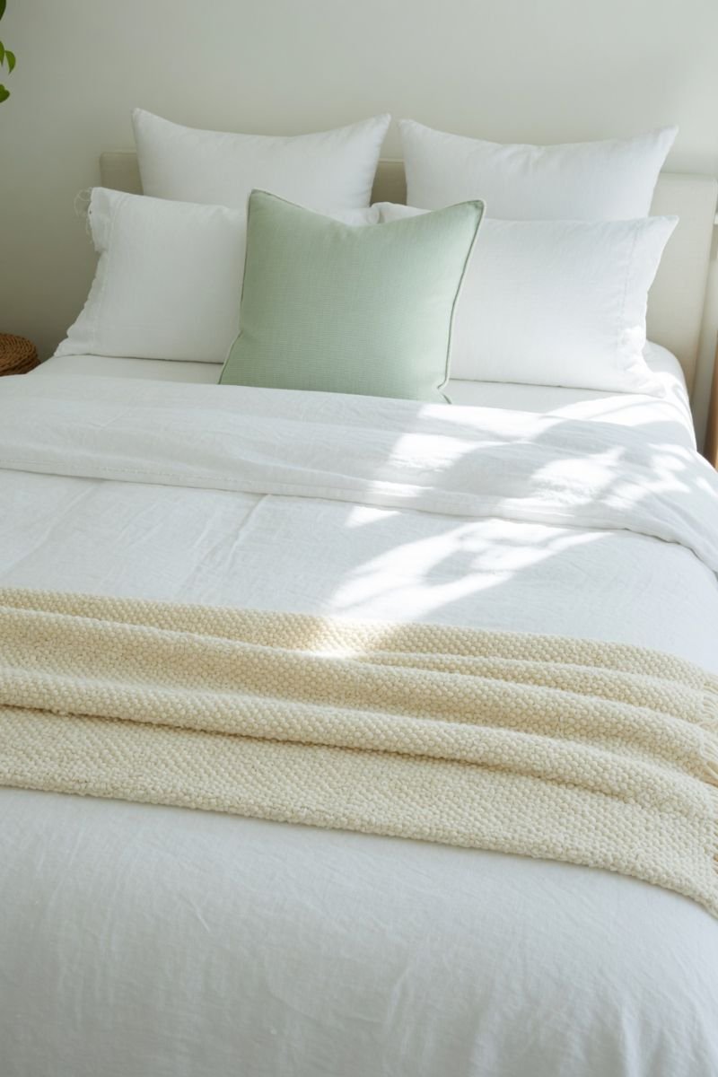 White linen bedding with waffle weave blanket on a bright summer bedroom bed