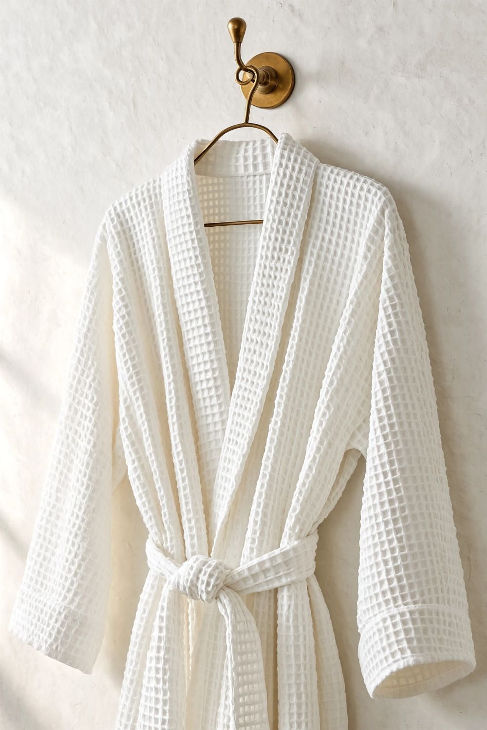 White linen robe hanging from a brass hook on a bathroom wall in a spa style bathroom