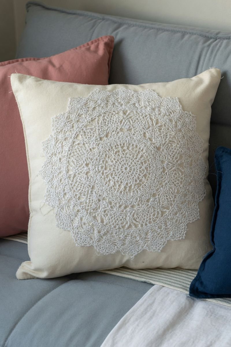 White throw pillow with round doily attached to front on a neutral sofa