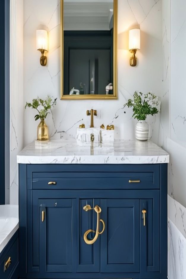 A navy blue bathroom vanity with brass hardware and a white marble countertop