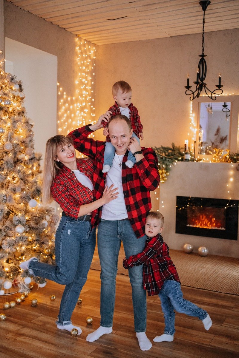 Family wearing matching plaid shirts and dark denim in front of a Christmas tree