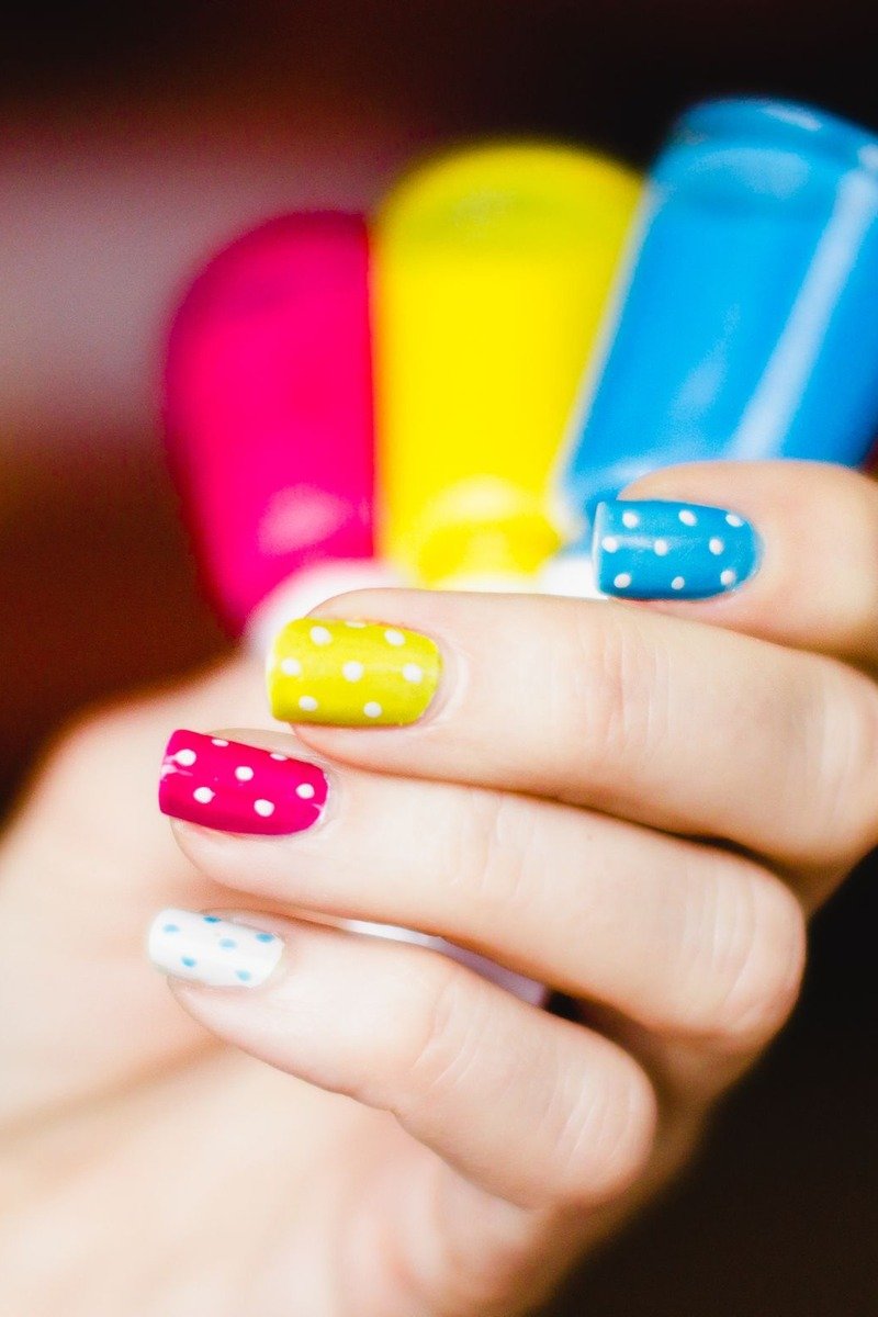 Short nails with multicolor polish and white polka dots, hand holding nail polish bottles