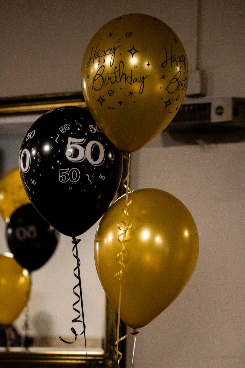 Gold and black glam birthday backdrop with balloons and a cake table
