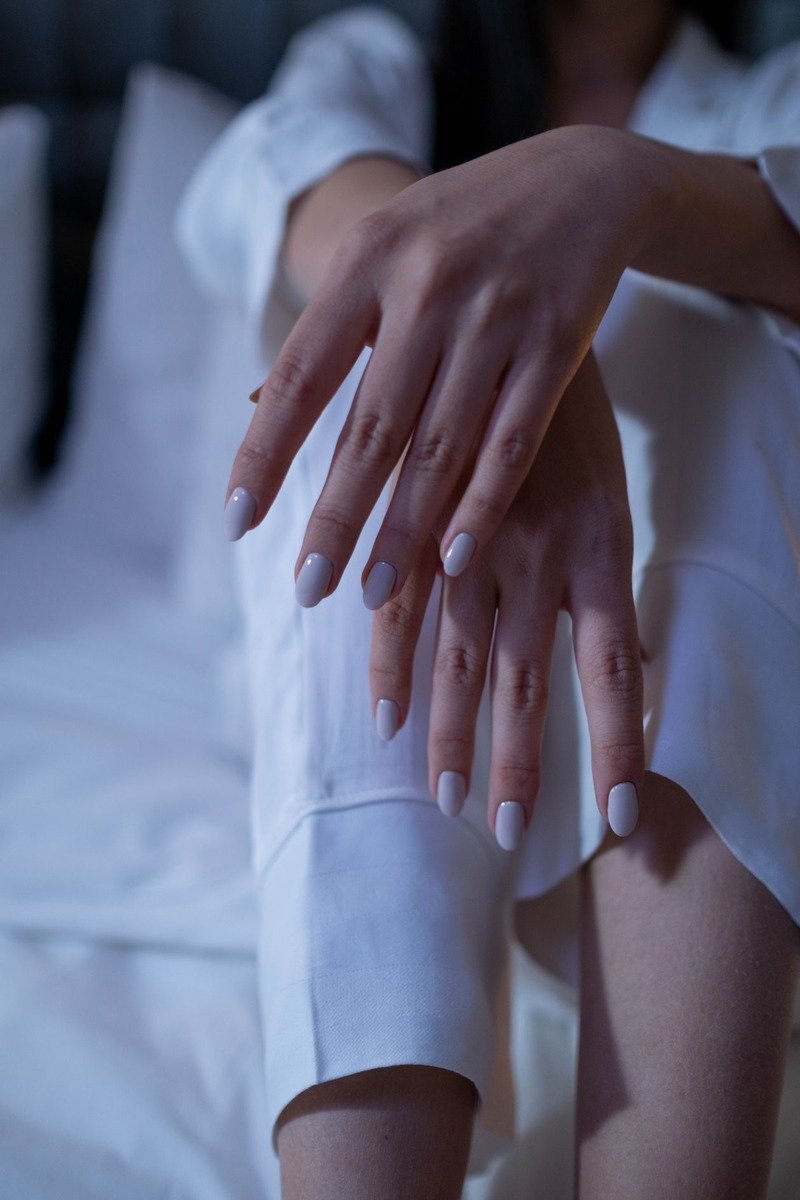 Sheer milky white nails, hands resting on white bedding in soft daylight
