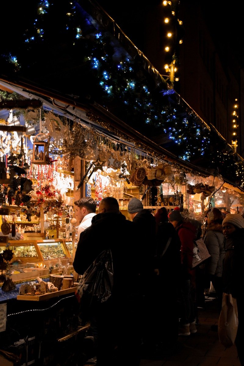 Crowds browsing wooden stalls strung with lights at a Bavarian Christmas market at night