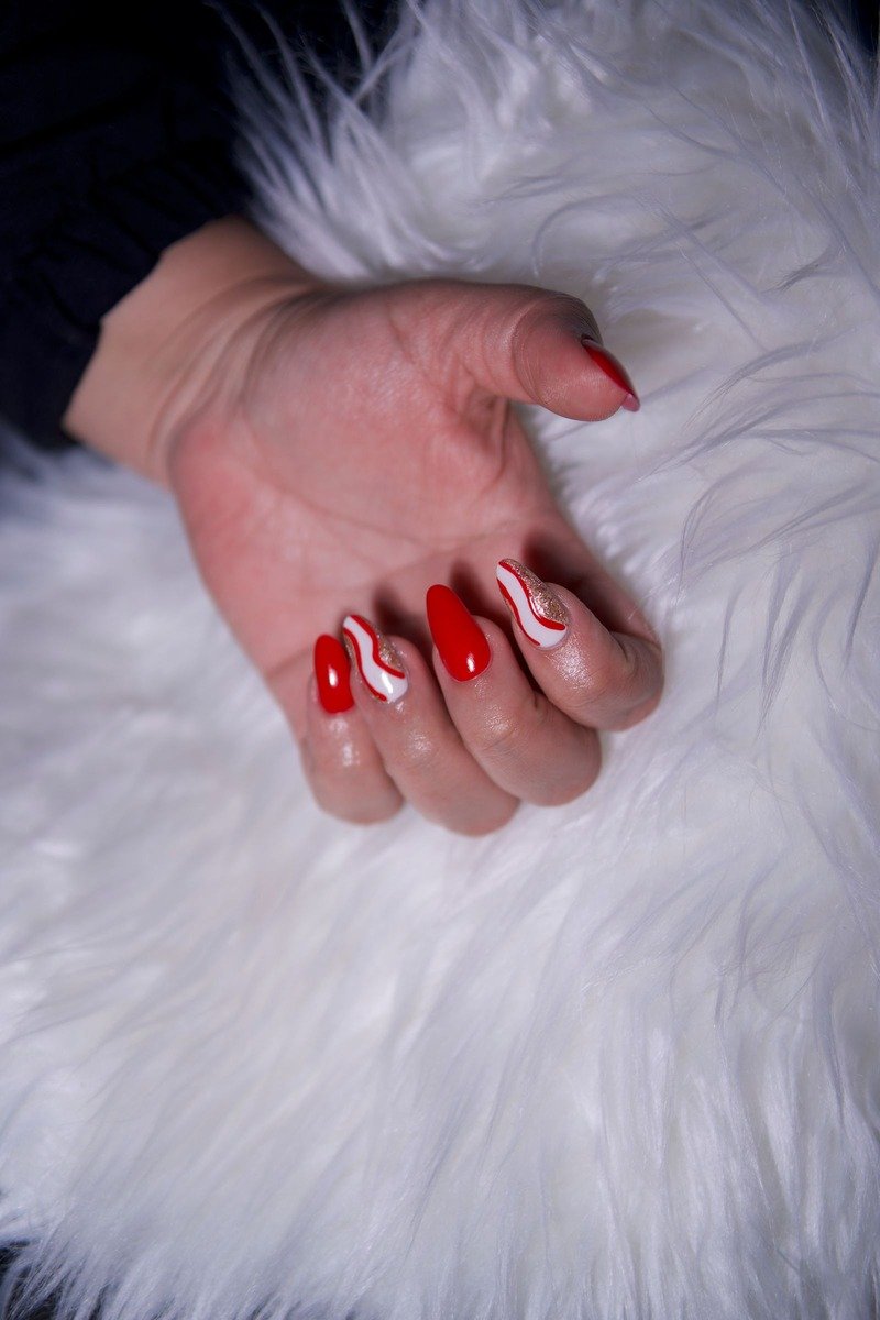 Red almond nails with white swirls and gold glitter accents