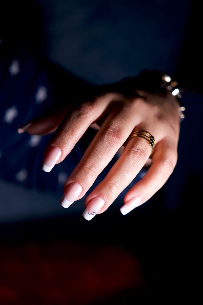 French manicure with gold rings and bracelet on dark background