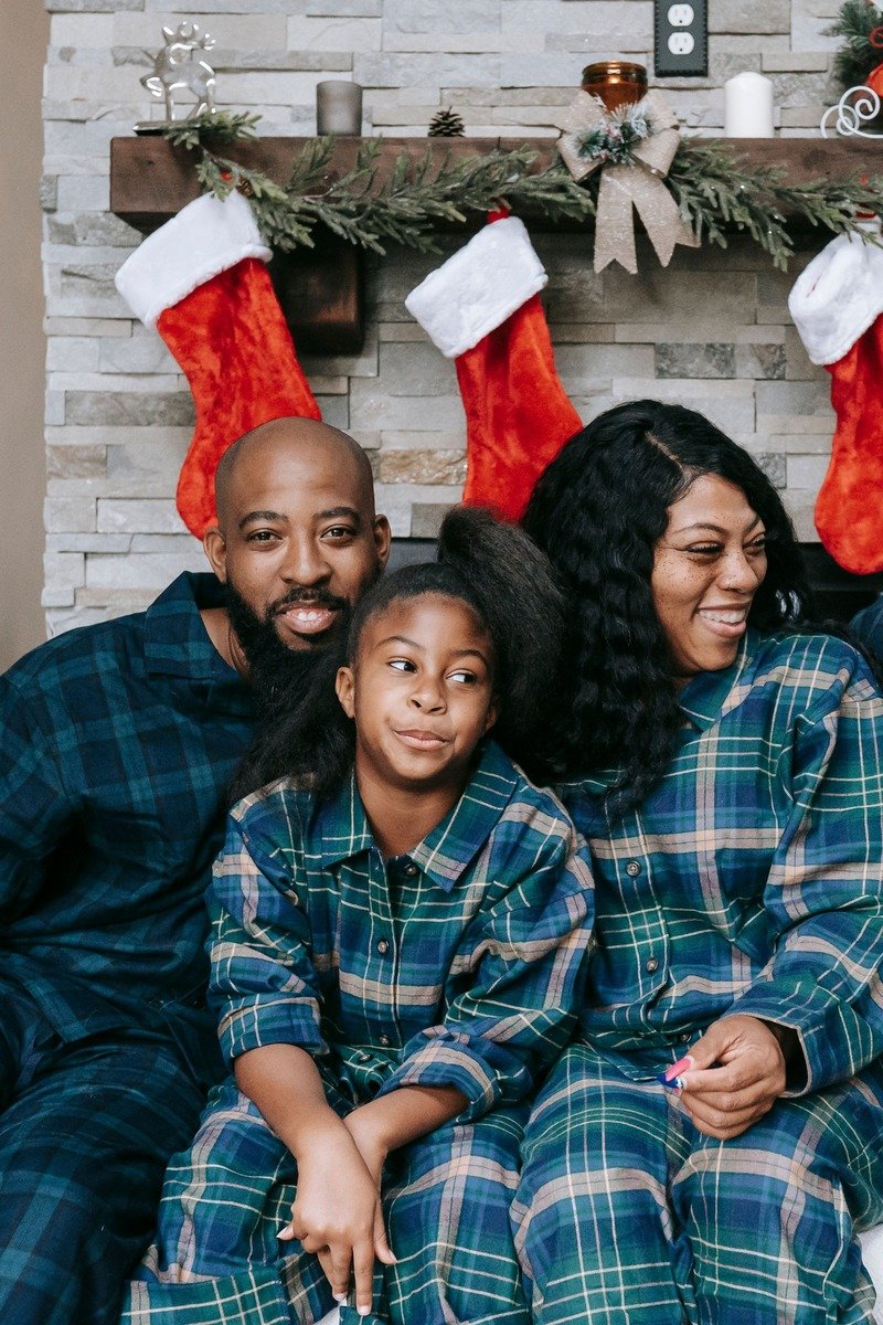 Family in buffalo check pajamas sitting by a fireplace