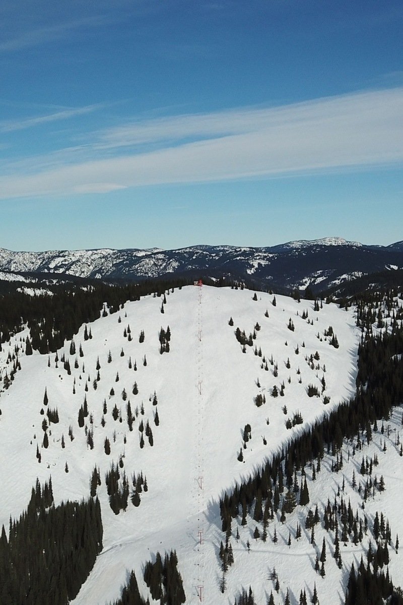 Aerial view of snowy ski slopes and lift lines above a mountain lake