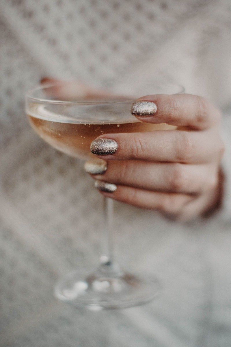 Champagne gold glitter short nails holding a champagne coupe