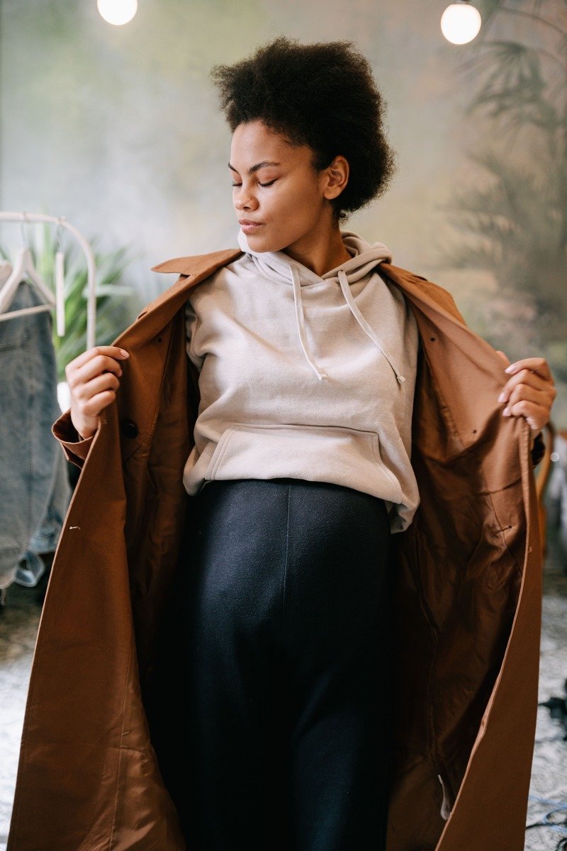 Woman over 40 in a hoodie layered under a tailored coat with jeans