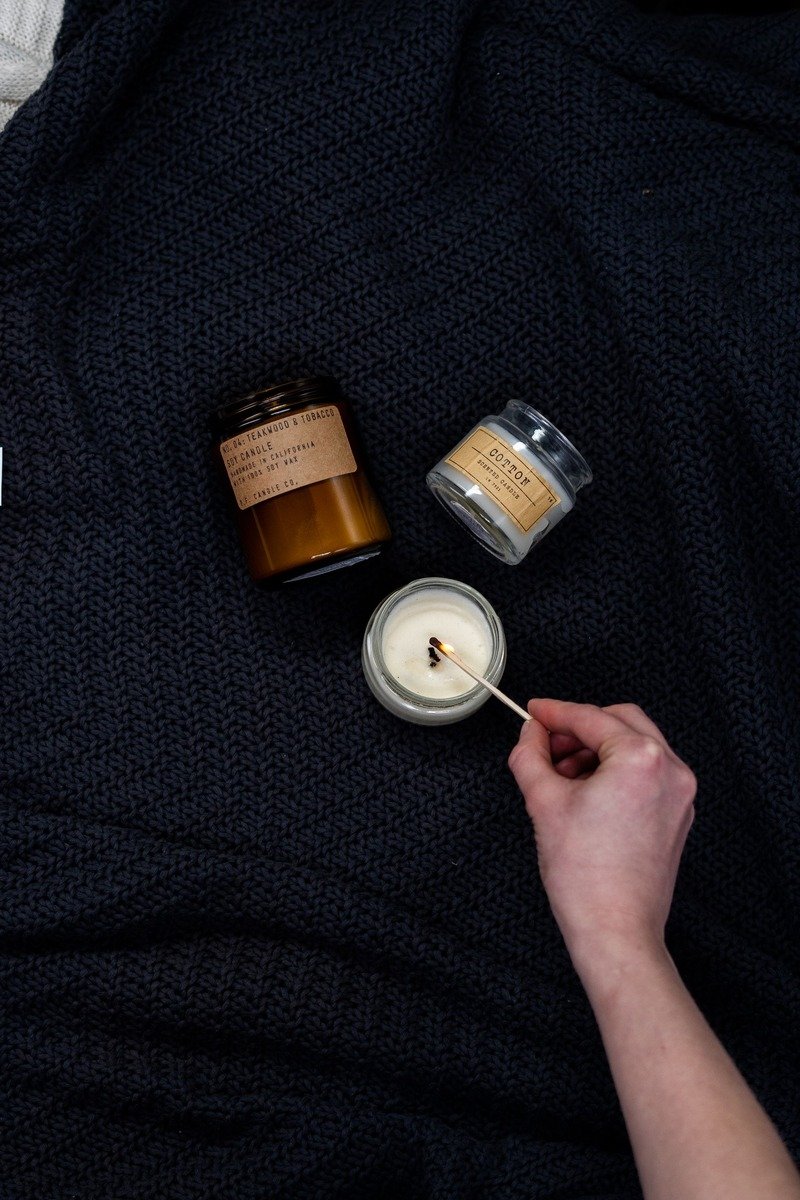 Jar candles on a knitted blanket being lit with a match