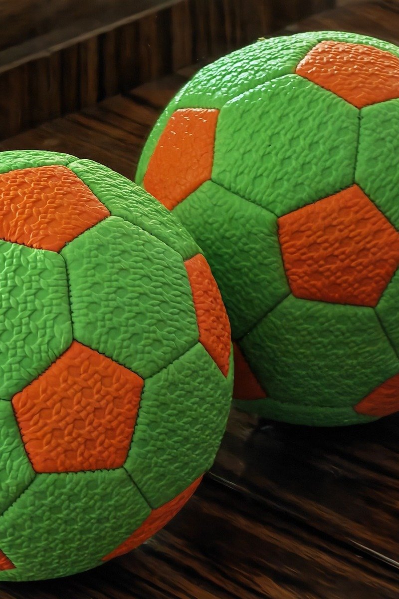 Two colorful soccer balls on a wooden surface