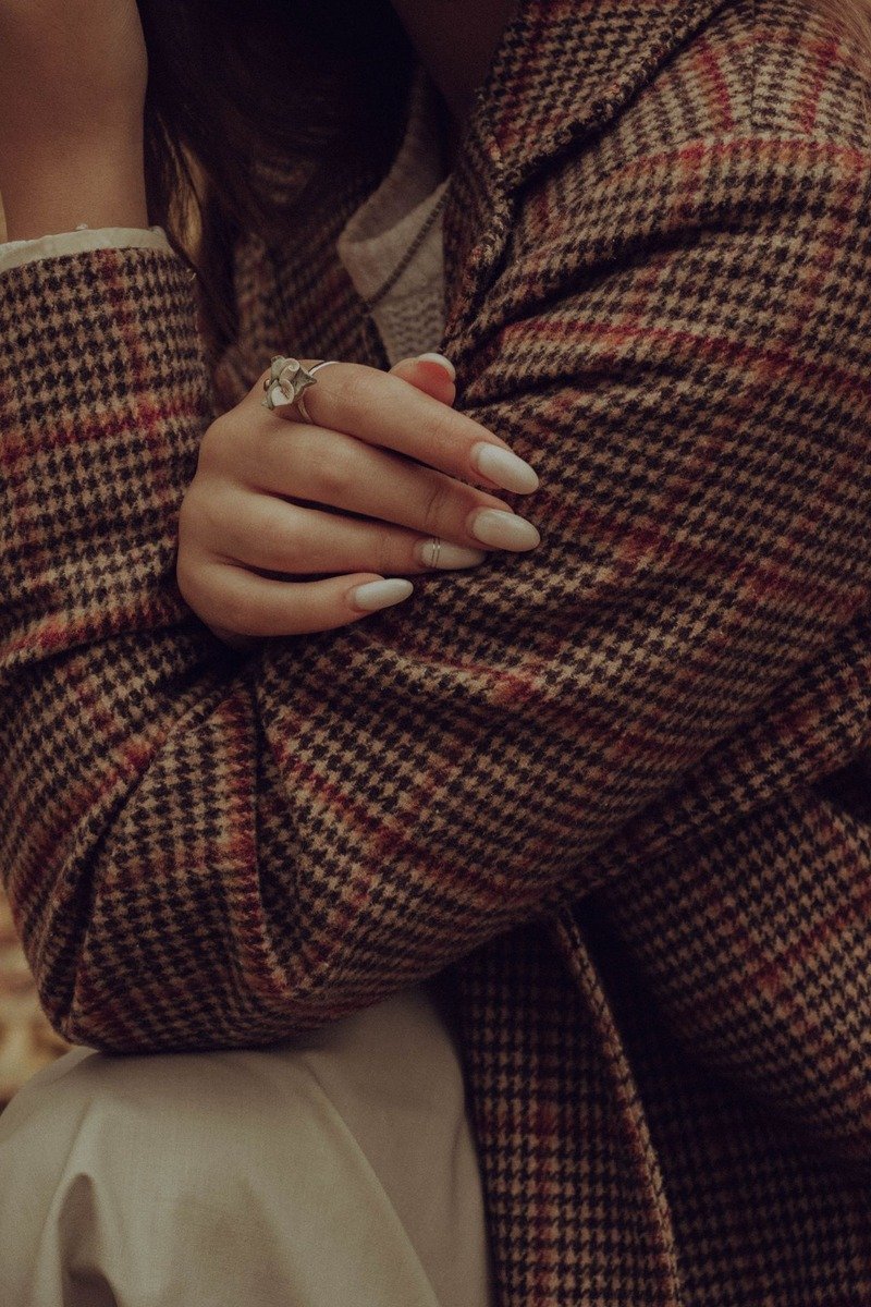 Glossy nude nails, hand resting on a checkered blazer, fashion editorial