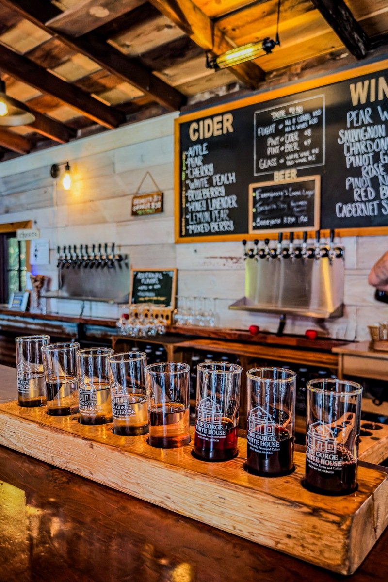 A tasting flight of eight small pours lined up on a wooden paddle at a taproom bar