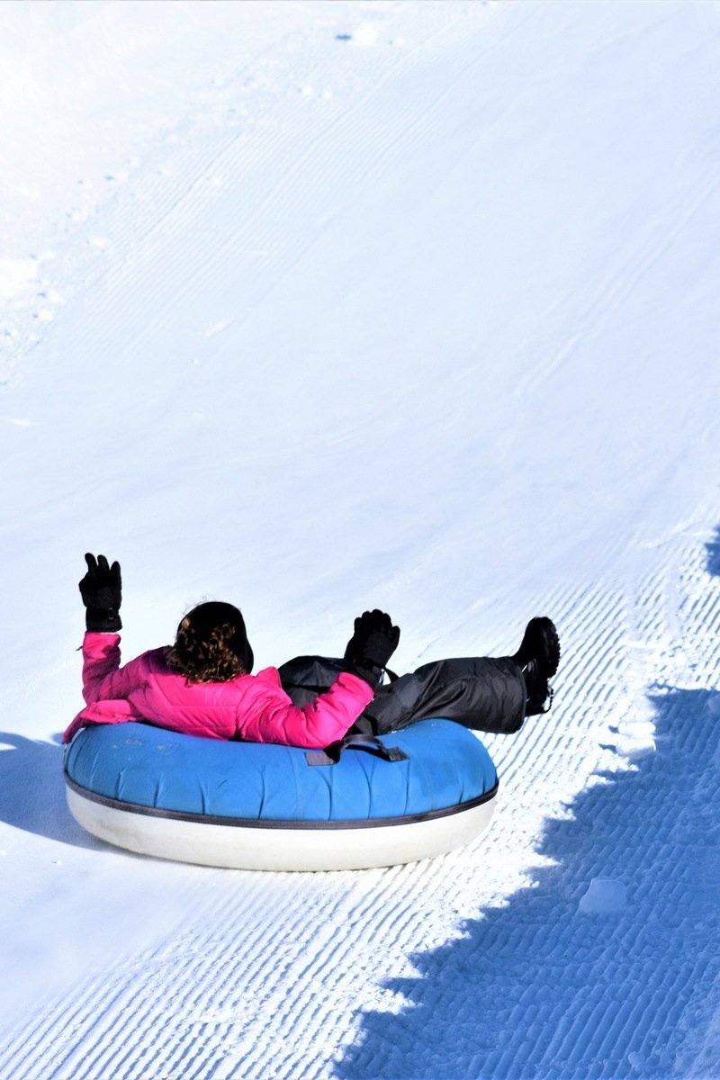 Snow tuber sliding down a groomed tubing lane with arms raised on a sunny winter day