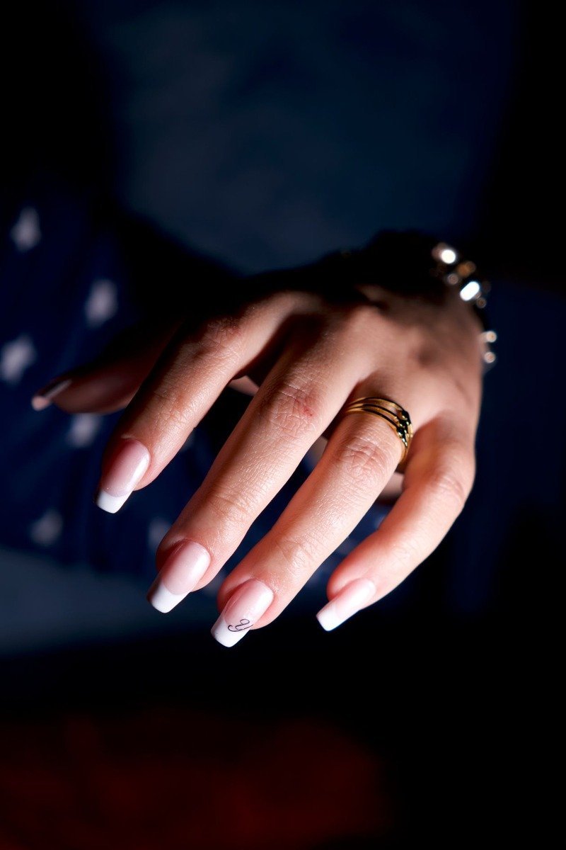 Long French-tip nails with gold jewelry on dark background