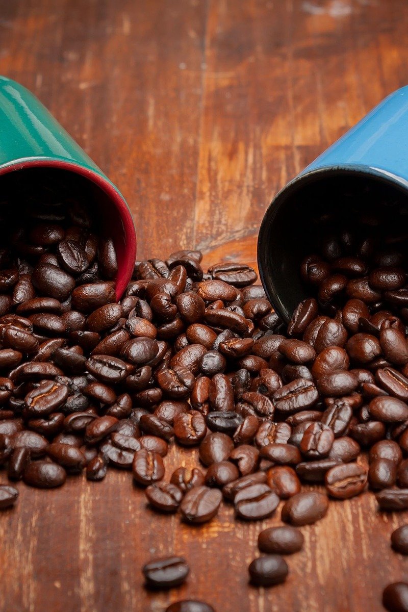 Two mugs with spilled roasted coffee beans on a wooden table