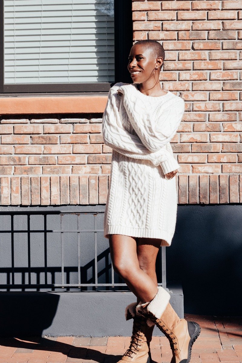 Woman in a sweater dress with boots standing by an office window