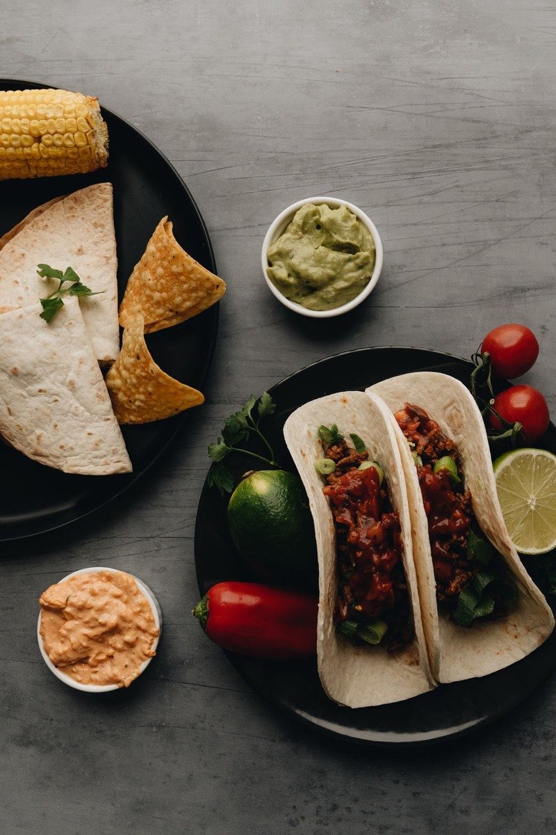 Tacos with salsa chips and guacamole on dark plates