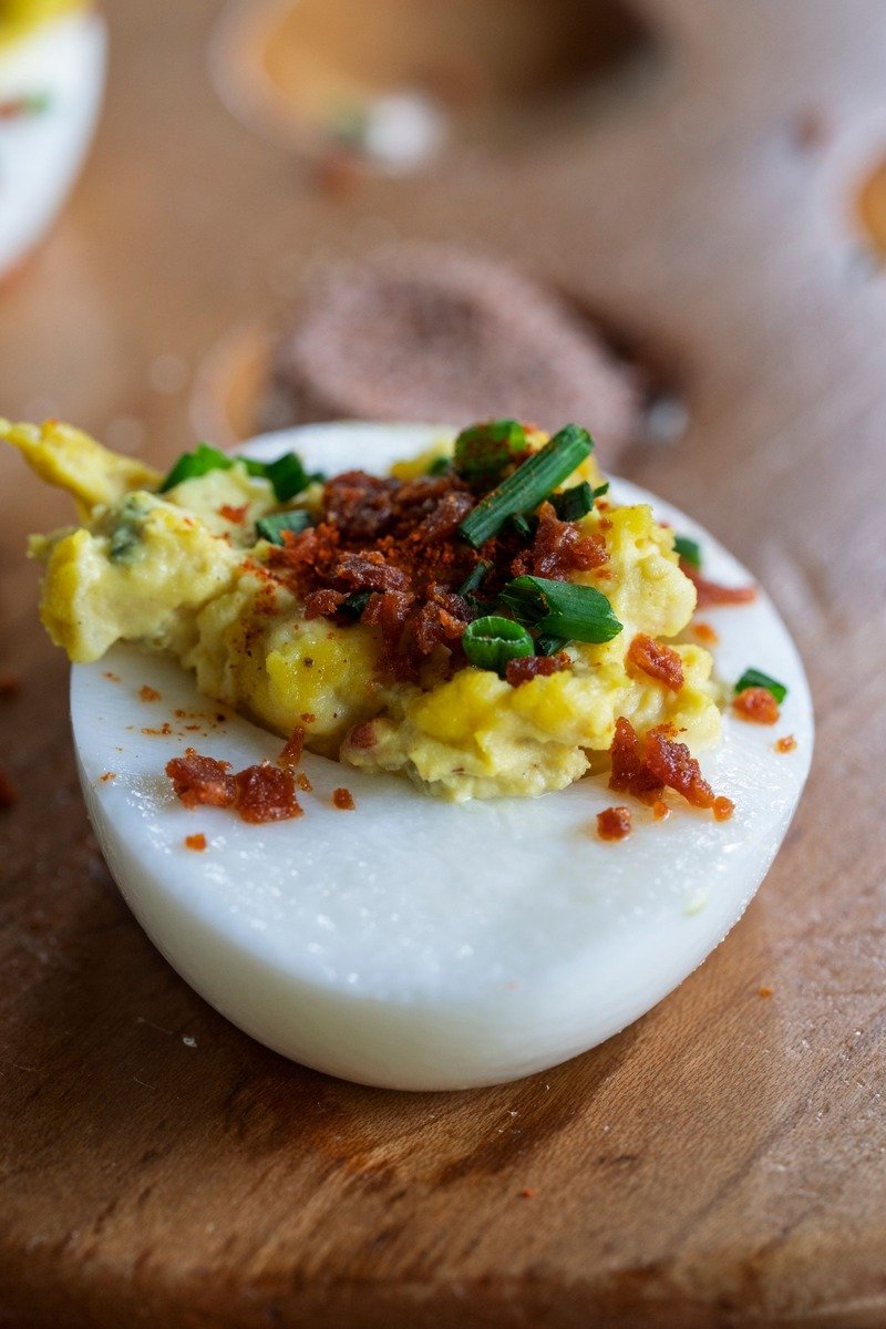 Deviled egg with paprika and bacon bits on a wooden board