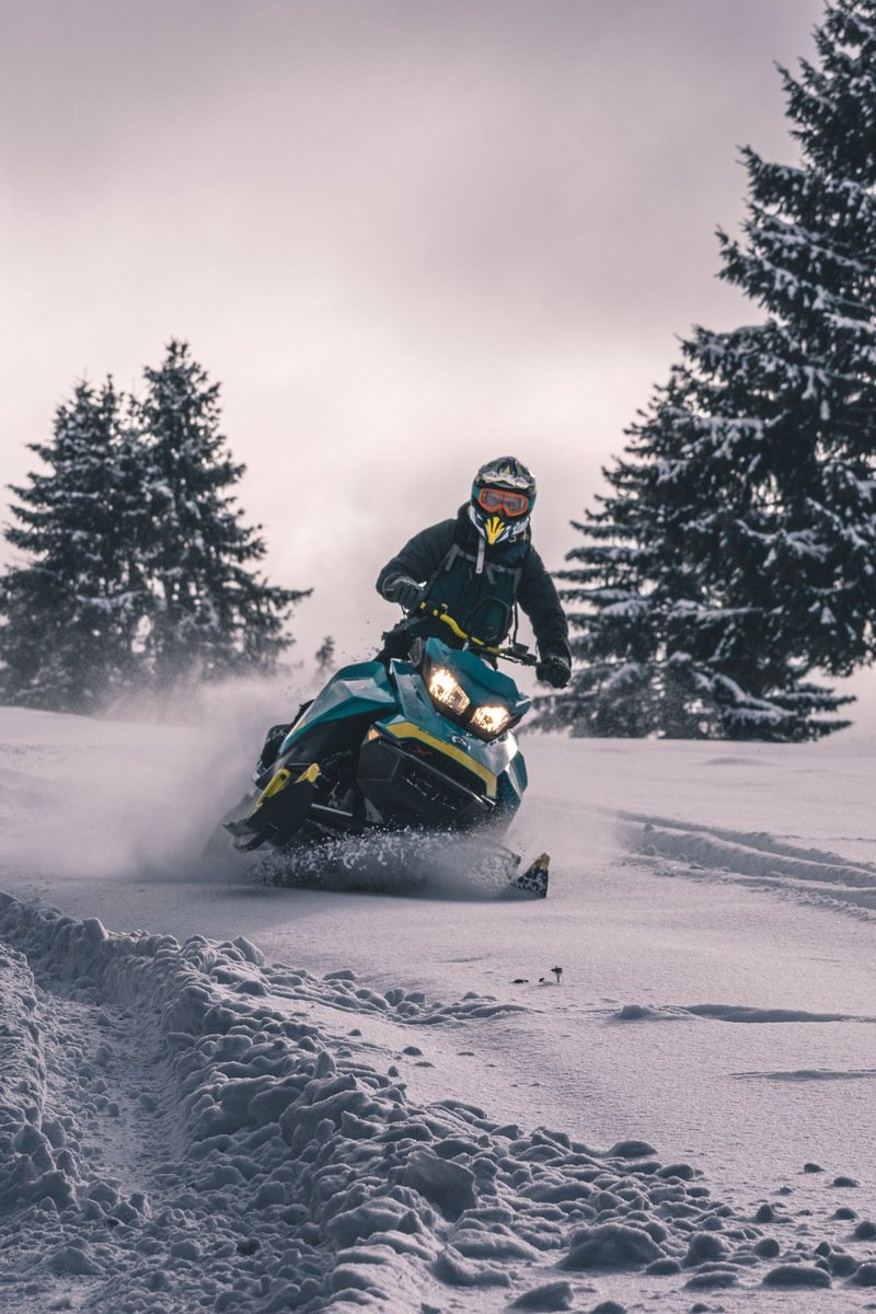 Snowmobiler carving through fresh powder past snow-covered evergreens