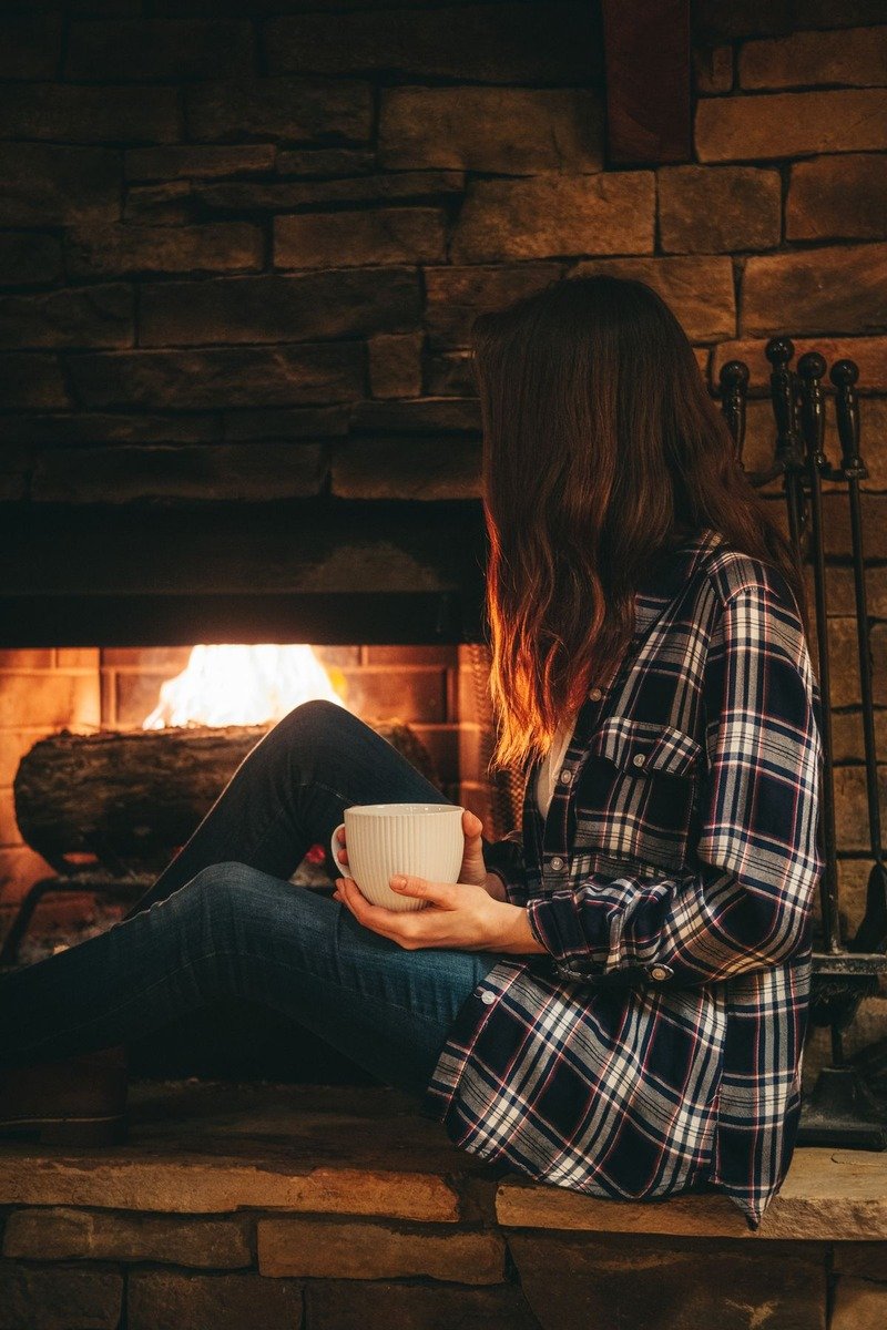 Woman in a flannel shirt and fleece-lined leggings by a fireplace