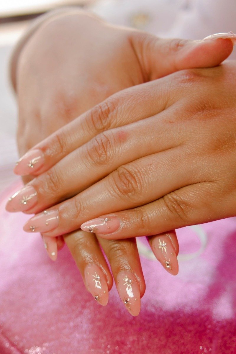 Nude almond nails with gold star line art and tiny crystals