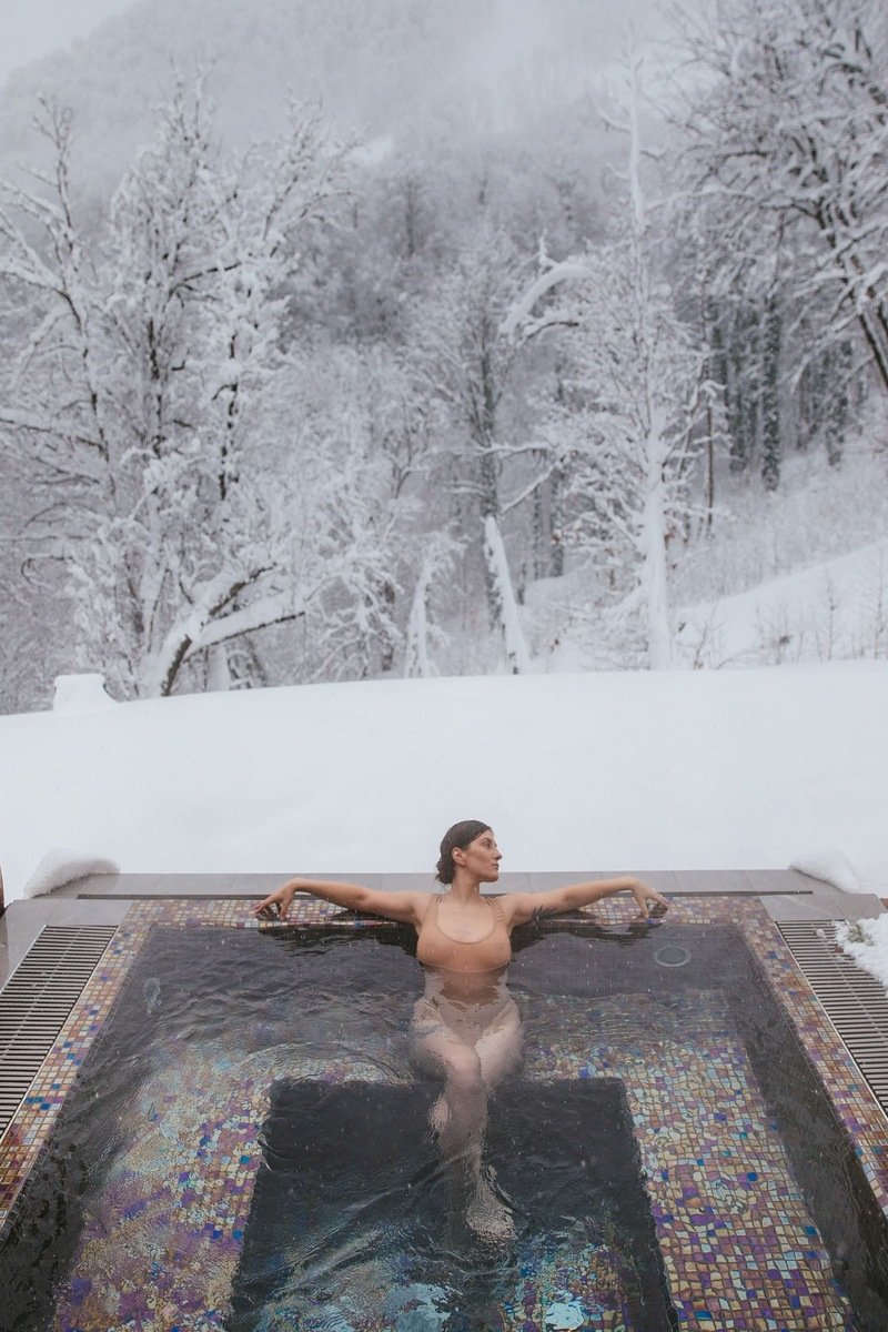 Woman soaking in an outdoor hot tub surrounded by snow-covered trees