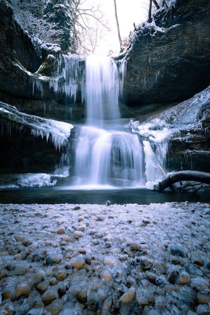 Frozen waterfall draped in icicles cascading through a snowy forest gorge